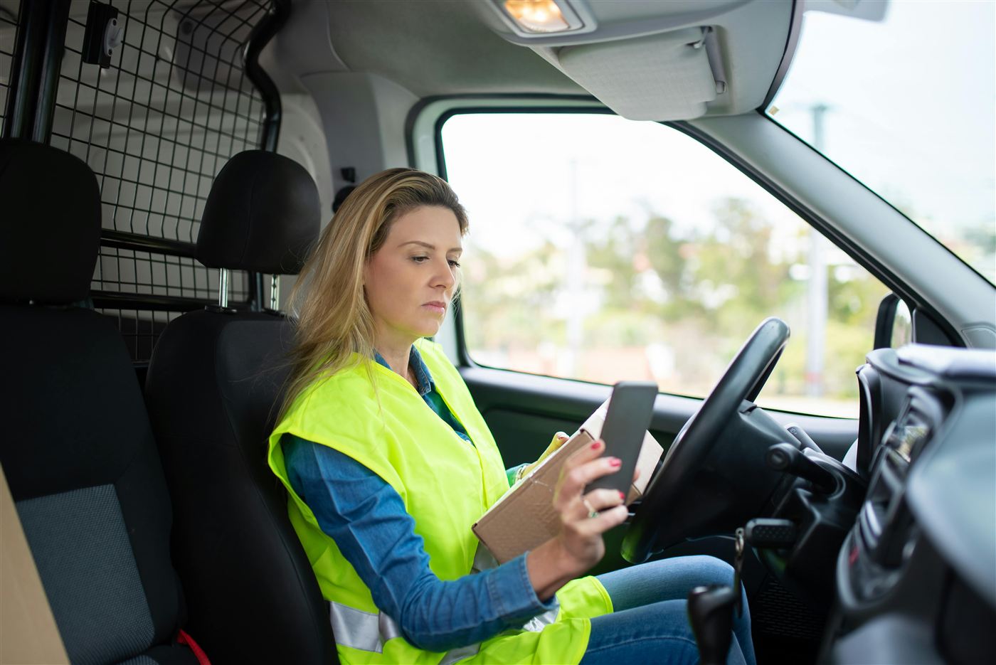 Delivery driver in a high-vis vest checking her phone in the van